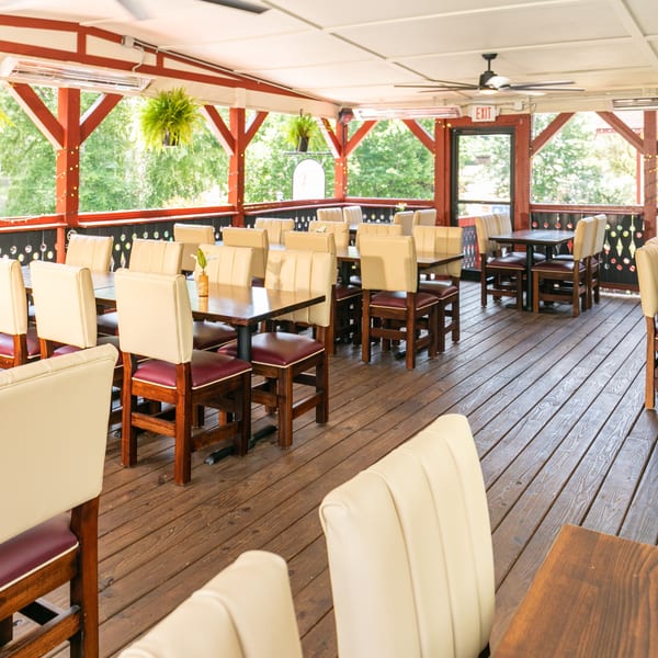 Outdoor restaurant patio with wooden floors, red beams, cream and maroon chairs, and hanging plants.