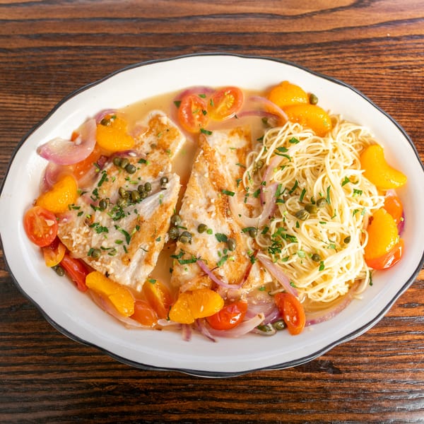 Two fish fillets with pasta, cherry tomatoes, orange segments, and capers in a light sauce.