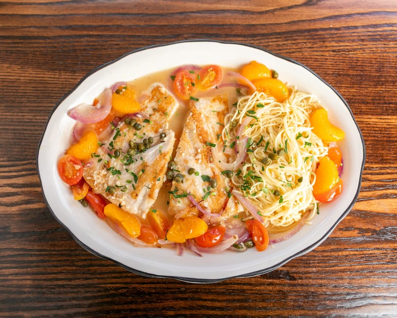 Two fish fillets with pasta, cherry tomatoes, orange segments, and capers in a light sauce.