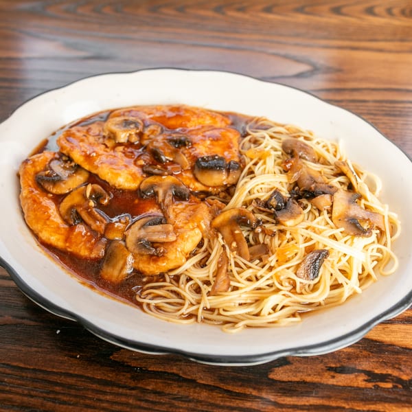 Chicken and mushrooms in a rich brown sauce, served with thin noodles on a white plate.
