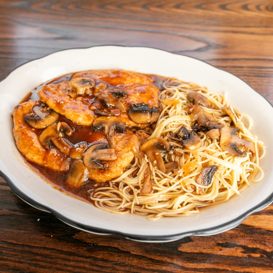 Chicken and mushrooms in a rich brown sauce, served with thin noodles on a white plate.
