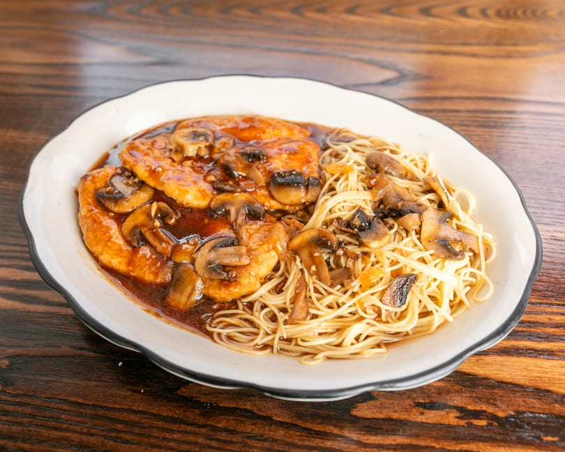 Chicken and mushrooms in a rich brown sauce, served with thin noodles on a white plate.