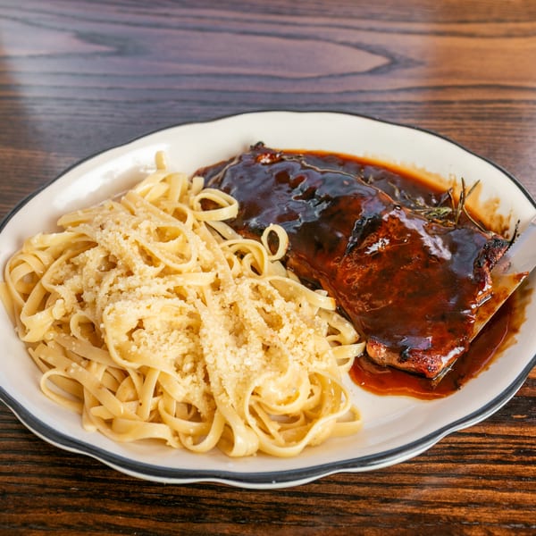 Plate of BBQ ribs with a rich sauce, rosemary sprigs, and a side of fettuccine pasta with parmesan.