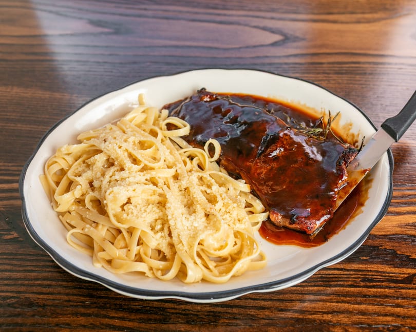 Plate of BBQ ribs with a rich sauce, rosemary sprigs, and a side of fettuccine pasta with parmesan.