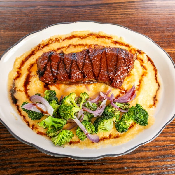 Grilled steak with balsamic glaze on a bed of polenta, garnished with broccoli and red onions.