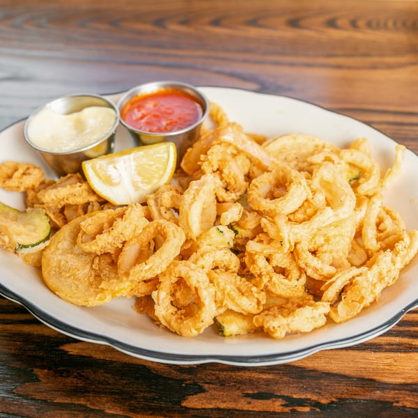 Crispy fried calamari and zucchini on a white plate with lemon, marinara, and aioli.