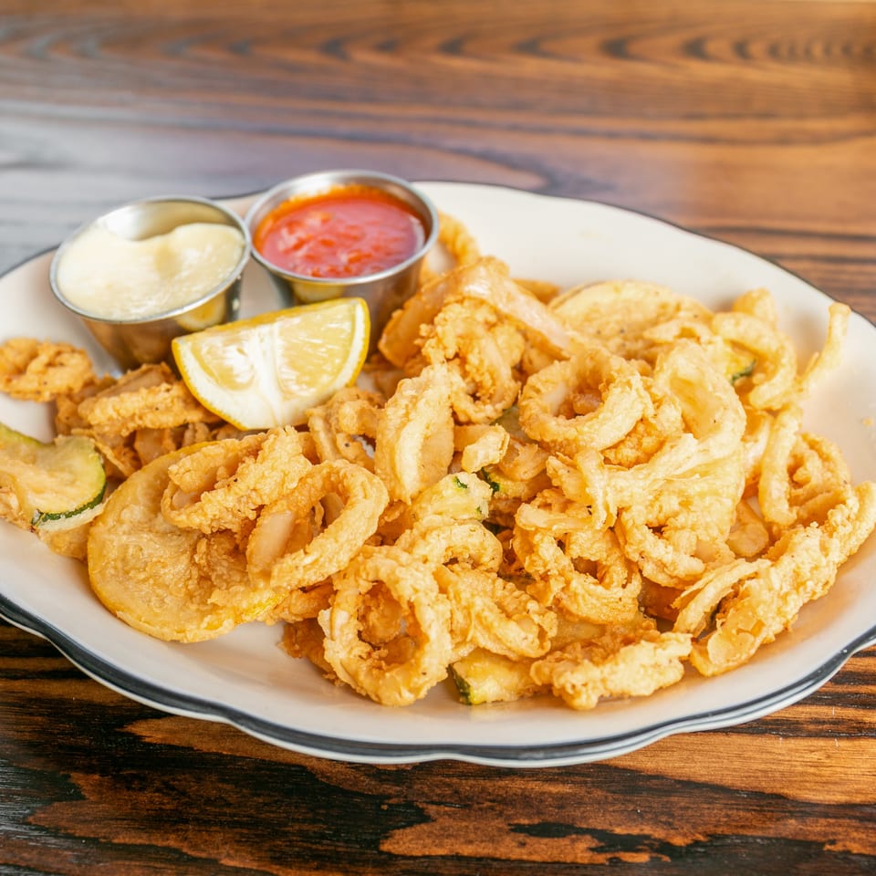 Crispy fried calamari and zucchini on a white plate with lemon, marinara, and aioli.