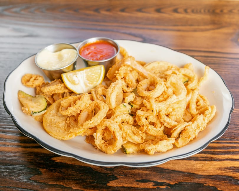 Crispy fried calamari and zucchini on a white plate with lemon, marinara, and aioli.