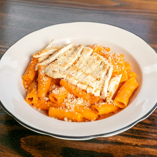 Rigatoni pasta with orange sauce, grilled chicken, and grated cheese in a white bowl.
