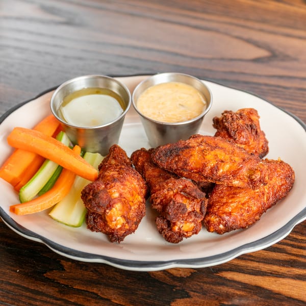 Crispy fried chicken wings with carrot and celery sticks, and two dipping sauces on a white plate.