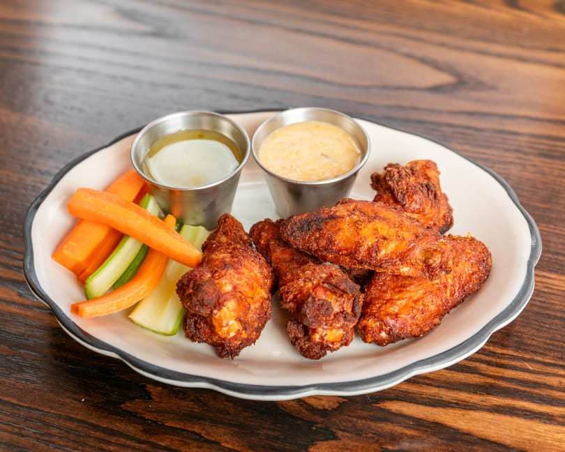 Crispy fried chicken wings with carrot and celery sticks, and two dipping sauces on a white plate.